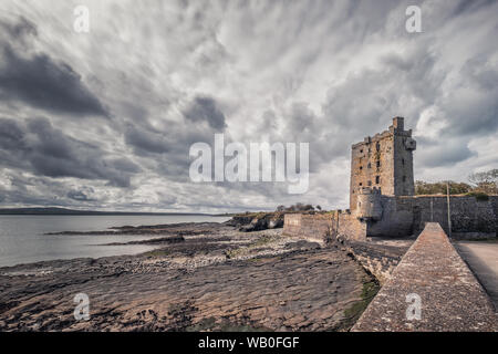 Dunkle Wolken hängen über den Ruinen von carrigaholt Burg, die die Mündung des Shannon in der Grafschaft Clare in Irland mit Blick auf Stockfoto