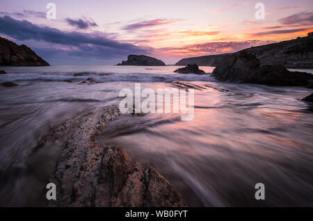 Bunte bewölkt Sonnenaufgang am Strand von Playa de la arnia mit dynamischem Kurven und bizarre Felsen, Liencres, Nordspanien Stockfoto