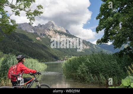 Schöne und aktive Seniorin, die mit dem e-Mountain-Bike im Tannheimer Tal am Haldensee, in Österreich, mit dem Dorf Tannheim unterwegs ist Stockfoto