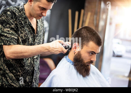 Die Frisur perfekt aussehen. Junger bärtiger Mann, Haarschnitt, Friseur, während im Stuhl sitzen im barbershop Stockfoto