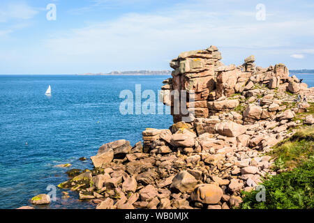 Granit felsenmeer Auf der rosa Granit Küste im Norden der Bretagne, Frankreich, mit einem kleinen Katamaran Segeln auf dem Meer in der Ferne. Stockfoto