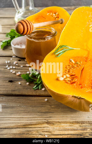 Hälften der rohen Kürbis butternut squash, mit Olivenöl, Gewürze und Zutaten zum Kochen auf rustikalen alten hölzernen Hintergrund. Nach oben Ansicht kopieren. Stockfoto