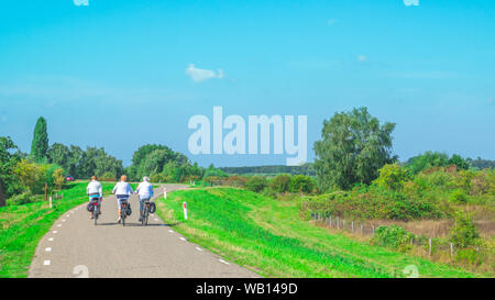 Drei unkenntlich Menschen Zyklus über einen Deich in einem typisch holländische Polderlandschaft in der ooijpolder in Gelderland Stockfoto