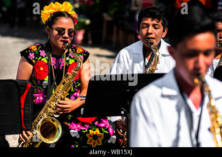 Ein mexikanisches Mädchen von zapotec Herkunft, tragen traditionelle Tehuana Kleid, spielt Saxophon während des Festivals in Juchitán de Zaragoza, Mexiko. Stockfoto