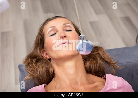 Attraktive, reife Frau, hypnotisiert beim Liegen auf dem Sofa Stockfoto