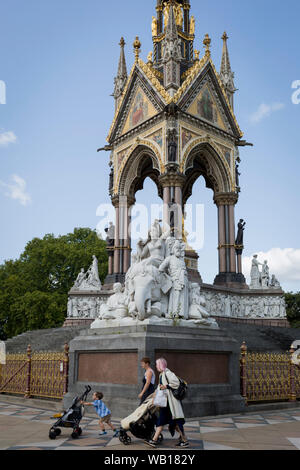 Mütter und Kinder zu Fuß vor der Golden Schmiedearbeiten an der Albert Memorial in Kensington Park, am 20. August 2019, in London, England. Das Albert Memorial, direkt nördlich der Royal Albert Hall in Kensington Gardens, London, wurde von Königin Victoria zum Gedenken an ihren geliebten Ehemann Prinz Albert, der im Jahr 1861 in Betrieb genommen. Von Sir George Gilbert Scott im Neugotischen Stil gestaltet, es hat die Form eines verzierten Baldachin oder Pavillon 176 Fuß hoch, im Stil einer gotischen Ziborium über dem Hochaltar der Kirche beherbergt eine Statue der Prinz auf der Südseite. Es dauerte über zehn Ihr Stockfoto