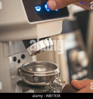 Extrahieren der Geschmack aus den Bohnen. Kaffeemühle mahlen gerösteten Bohnen in Pulver. Barista grind Kaffee Bohnen auf Kaffeemaschine. Frischem Boden coff Stockfoto