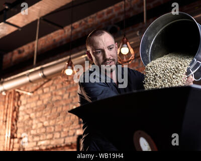 Mann gießen grüne Kaffeebohnen in Kaffeeröster Stockfoto