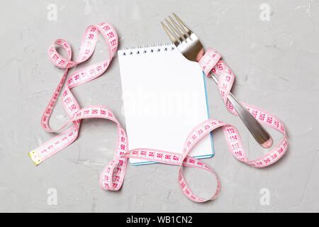 Rosa Maßband, geöffnet Notebook und Gabel auf Zement Hintergrund mit leeren Raum für Ihre Idee. Blick von oben auf die gesunde Lebensweise Konzept. Stockfoto