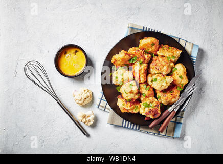 Frittierte Blumenkohlröschen serviert auf einer schwarzen Platte auf einer konkreten Tabelle mit Zutaten, von oben betrachten, Nahaufnahme, flatlay Stockfoto