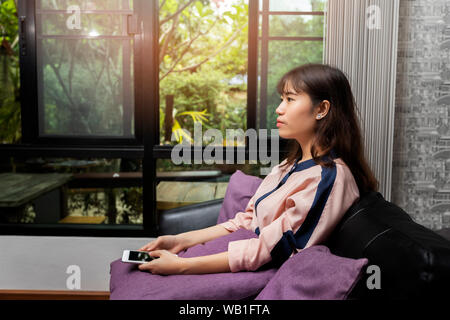 Schöne junge asiatische Frau mit Handy beim Sitzen auf dem Sofa Stockfoto