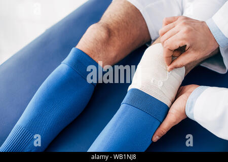 7/8-Ansicht des Physiotherapeuten, elastische Bandage am Bein der Fußballspieler Stockfoto