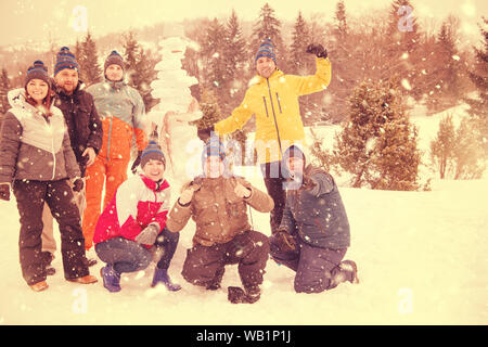 Gruppe Porträt der jungen glücklich Geschäftsleute nach einem Wettbewerb posiert mit fertigen Schneemann beim Genießen verschneiten Wintertag mit Schneeflocken um Stockfoto