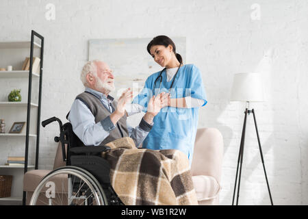 Krankenschwester im Gespräch mit Behinderten und glücklich, grauhaariger Mann im Rollstuhl Stockfoto