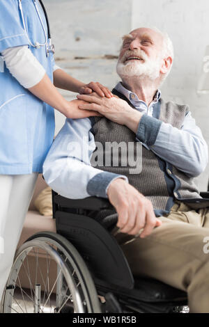 Doktor, Hände halten mit fröhlichen und behinderte ältere Menschen im Rollstuhl Stockfoto