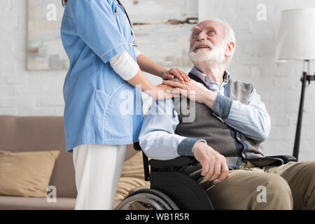 Glücklich und behinderte ältere Menschen im Rollstuhl Hand in Hand mit dem Arzt Stockfoto