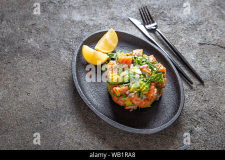 Peruanische NIKKEI ESSEN. Lachs, Avocado ceviche auf schwarze Platte, schwarzen Hintergrund, Ansicht von oben Stockfoto