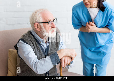 7/8-Ansicht der Krankenschwester zu sprechen, grauhaariger Mann mit Stock Stockfoto