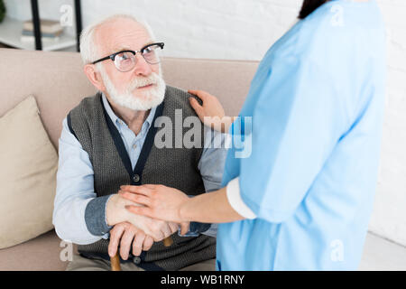 7/8-Ansicht der Krankenschwester, die Hände auf grauhaariger Mann Stockfoto