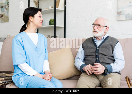 Gerne Krankenschwester sitzen auf der Couch, grauhaariger Mann suchen Stockfoto
