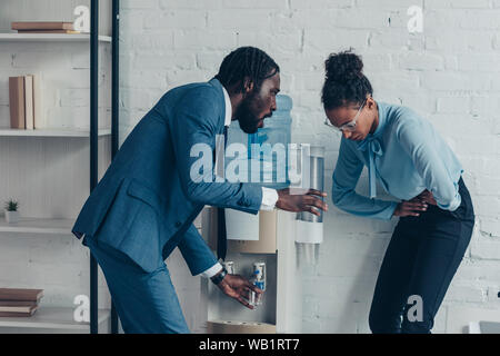 Afrikanische amerikanische Manager geben Glas Wasser ziemlich Kollegen leiden unter Bauchschmerzen sorgen Stockfoto
