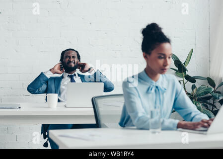 Afrikanische amerikanische Geschäftsmann leidet unter Kopfschmerzen beim Sitzen im Büro in der Nähe der hübschen Manager Stockfoto
