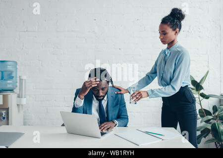 Ziemlich afrikanische amerikanische Manager stehen in der Nähe von Unternehmer leiden unter Kopfschmerzen am Arbeitsplatz Stockfoto