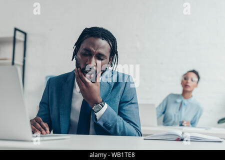 Unglückliche Unternehmer leiden unter Zahnschmerzen beim Sitzen im Büro in der Nähe der hübschen Manager Stockfoto