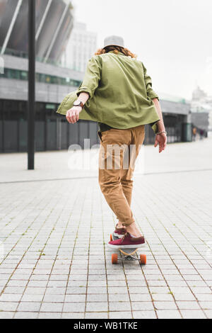 Rückansicht des Menschen in Freizeitkleidung reiten auf Skateboard auf der Straße Stockfoto