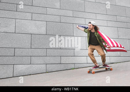 Glückliche Menschen in Freizeitkleidung mit amerikanischer Flagge reiten auf Skateboard Stockfoto