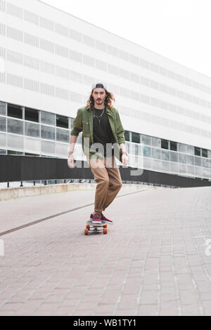 Schöner Mann in Freizeitkleidung reiten auf Skateboard auf der Straße Stockfoto