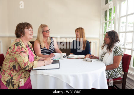 Informell gekleideten Frauen im Gespräch saßen um einen Tisch Stockfoto