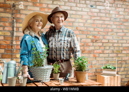 Ältere Frau im Strohhut mit Ehemann in der Nähe von grünen Pflanzen Stockfoto