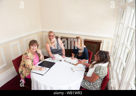 Informell gekleideten Frauen im Gespräch saßen um einen Tisch Stockfoto