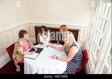 Informell gekleideten Frauen im Gespräch saßen um einen Tisch Stockfoto