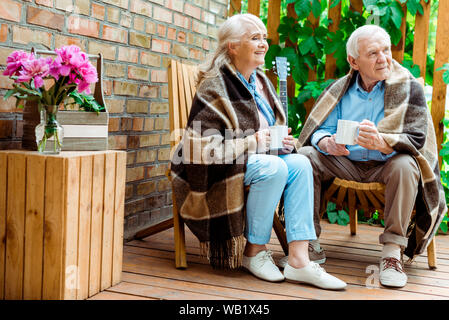 Freundliche ältere Frau und Mann sitzen auf der Terrasse und halten Cups Stockfoto