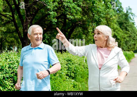 Überrascht ältere Frau zeigt mit dem Finger, während er in der Nähe von Ehemann in Park Stockfoto