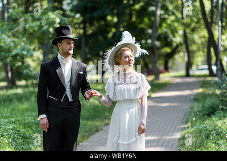 Der Mann und die Frau in der viktorianischen Hüte halten sich an den Händen, während draußen in der Nähe von grünen Bäumen, Stockfoto