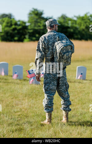 Militärische Mann, amerikanische Flagge in der Nähe von grabsteinen im Friedhof Stockfoto