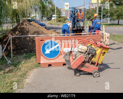 Odessa, Ukraine - 22. August 2019: Straße Arbeit auf dem Bürgersteig. Warnung Verkehrszeichen auf der Zaun um die Grube auf der Straße. Bagger gräbt ein Graben für Stockfoto