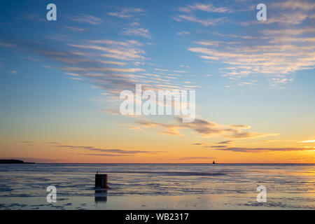 Die Sonne über einen gefrorenen Hafen und ein Eis angeln shack in ländlichen Prince Edward Island, Kanada. Leuchtturm am Horizont. Stockfoto