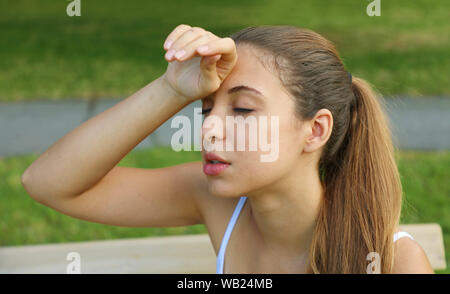 Attraktive Frau im Park sitzen mit starken Kopfschmerzen. Portrait von schönen Mädchen berühren ihre Stirn Stress oder Schmerzen. Stress oder Kopfschmerzen. Stockfoto
