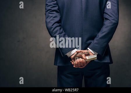 7/8-Ansicht von Handschellen Mann in formale Abnutzung Holding bestechen auf Grau Stockfoto