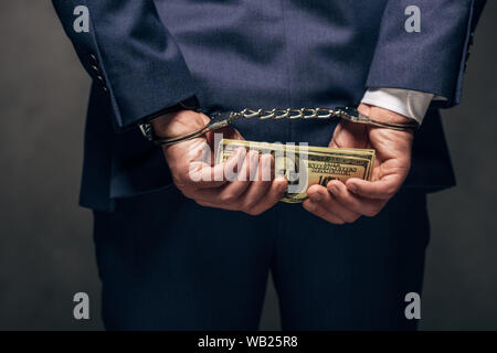 7/8-Ansicht von Handschellen Mann in Anzug Holding bestechen auf Grau Stockfoto