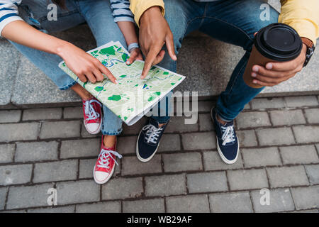 7/8-Ansicht der rassische Bi - Mann zeigte mit dem Finger auf der Karte in der Nähe von Frau sitzt auf der Treppe Stockfoto