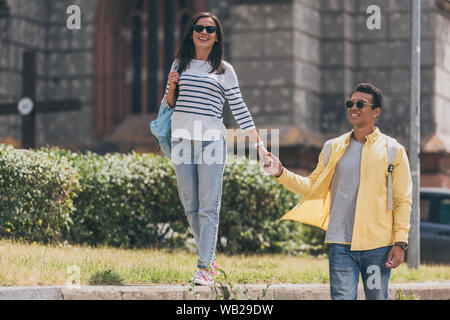 Multirassischen Mann in Sonnenbrille mit Frau halten sich an den Händen und Laufen Stockfoto