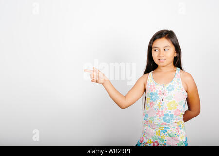 Ein 9-jähriges Mädchen ist auf der linken Seite. Sie steht vor einer weißen Wand. Sie lächelt. Sie hat lange dunkle Haare. Sie hat Hispanic featu Stockfoto