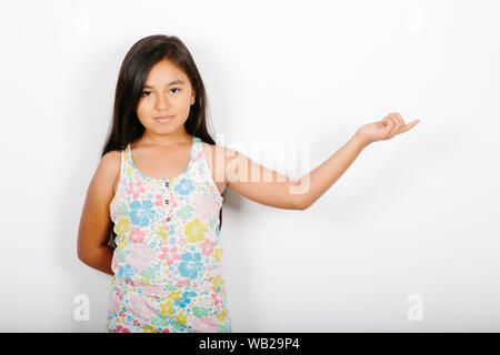 Ein 9-jähriges Mädchen ist auf der linken Seite. Sie steht vor einer weißen Wand. Sie hat einen neutralen Ausdruck. Sie hat lange dunkle Haare und hisp Stockfoto
