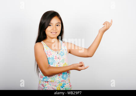 Ein 9-jähriges Mädchen ist auf der linken Seite. Sie steht vor einer weißen Wand. Sie lächelt. Sie hat lange dunkle Haare. Sie hat Hispanic featu Stockfoto