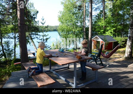 Zwei junge blonde Jungen zeichnen und crayoning an den hölzernen Tisch im Sommerhaus am See Sarkjarvi, Finnland. Stockfoto